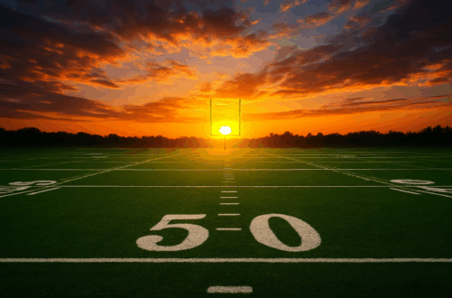 A wide view of an empty football field at sunset, seen from the 50 yard line. The sun sits perfectly centered between the goalposts on the far end of the field, casting a warm orange and red glow across the sky. Soft clouds stretch overhead, and the bright green turf contrasts with the dramatic sunset behind the tree line.