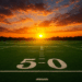 A wide view of an empty football field at sunset, seen from the 50 yard line. The sun sits perfectly centered between the goalposts on the far end of the field, casting a warm orange and red glow across the sky. Soft clouds stretch overhead, and the bright green turf contrasts with the dramatic sunset behind the tree line.