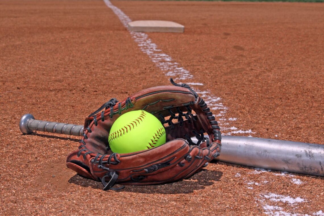Softball field with brown glove, silver bat, and yellow softball.