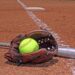 Softball field with brown glove, silver bat, and yellow softball.